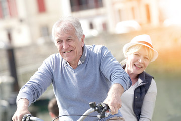 Senior couple having fun riding bike in tourist area