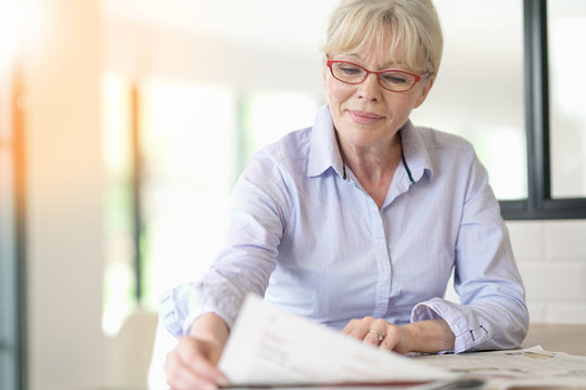 Senior woman with eyeglasses reading newspaper at home
