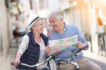 Senior couple riding bikes and reading map in tourist area - Powered by Adobe