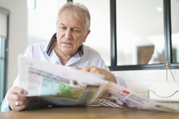 Senior man at home reading newspaper