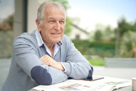 Senior Man Reading Newspaper Outside In Yard