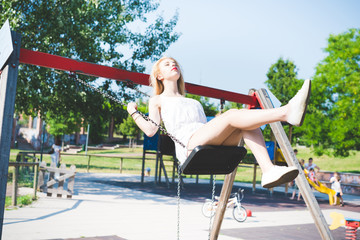 Young beautiful woman in a city park playing swing - enthusiasm, happiness, childhood concept
