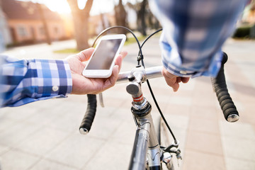 Senior man with smartphone riding bicycle in town.