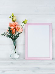 Flowers in vase and a photo frame on a wooden background.