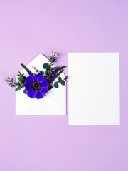 Blue flower in envelope and white sheet on violet background.