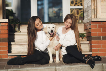 Fototapeta premium Young,beautiful women with long, straight,blond hair, beautiful smiles,are dressed in black leggings,posing outdoors in the spring,sitting in the city with their friend,dog,breeds a golden retriever