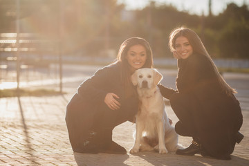 Young,beautiful women with long, straight,blond hair, beautiful smiles,are dressed in black leggings,posing outdoors in the spring,sitting in the city with their friend,dog,breeds a golden retriever