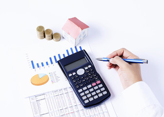 Hand holding pen and calculator and house paper and coins stack and business chart