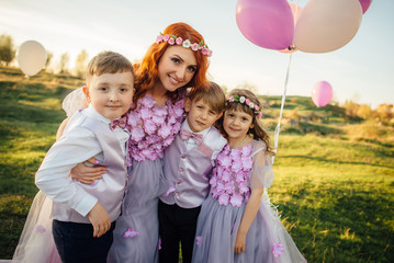 Young red-haired woman with her children in smart clothes playing with balloons in the park