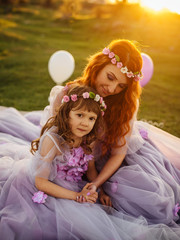 Young red-haired mother with her daughter resting on nature in the sun