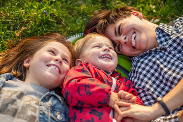 Fototapeta premium Mom and two kids lie on the grass in the park, laugh, spring, family