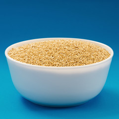 Raw white quinoa in a bowl on blue background