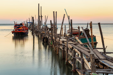 Old wood bridge for small fishing boat in the sea with sunset
