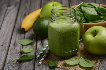 Green smoothie with apple, banana, avocado and spinach on rustic  wooden background. 