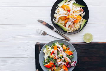 salad and pasta with seafood on wooden background