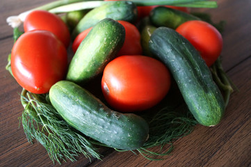 Colorful close up photo of vegetables as cucumbers, oval tomatoes, dill and long white bunching evergreen onion from garden on the dark wood finish table