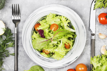 The dietary mixed greens salad (mesclun, mache, lettuce) and cherry tomatoes in a bowl on a light background