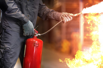 Naklejka premium Man using fire extinguisher fighting fire closeup photo.