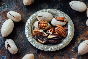 Pecan nuts on metal plate over black rustic surface.
