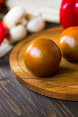Kumato tomatoes on wooden board surrounded by vegetables.