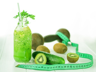 A bottle of smoothie with cucumber, kiwi and banana slices on white wooden table.