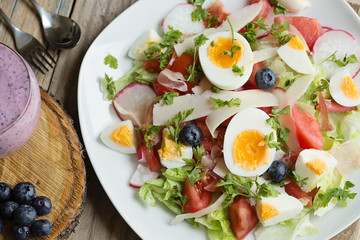 Chia and berries milk smoothie and fresh mixed leaves salad with boiled egg and vegetable, decorated with blueberries and parmesan shavings, view from above, close-up photo