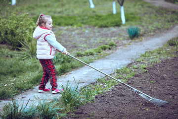 Raking in the Garden. Young girl play with rake.