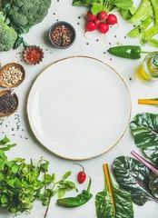 Fotobehang Fresh raw greens, unprocessed vegetables and grains over light grey marble kitchen countertop, wtite plate in center, top view, copy space. Healthy, clean eating, vegan, detox, dieting food concept © sonyakamoz
