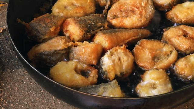 Frying hake fish outdoors on picnic, close up of frying pan with oil and fish slices