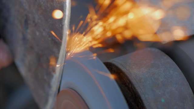 A man sharpens an ax on a machine with sparks.
