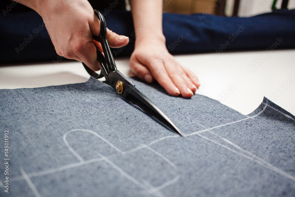 Wall mural hands of seamstress cutting a jeans fabric with scissors on white table