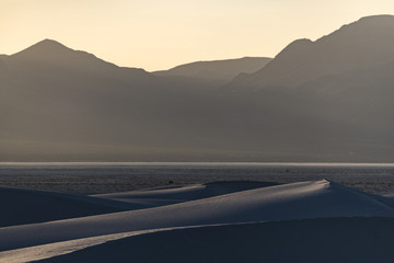 Golden hour with sand dunes against a desert mountain range