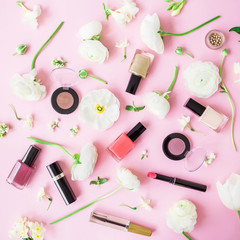 Obraz na płótnie Canvas Feminine desk with cosmetics, lipstick, nail polish, eye shadows and white flowers on pink background. Flat lay, top view. Beauty background