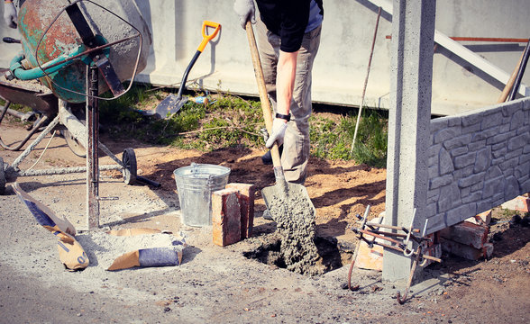 Pour concrete on the foundation of the fence with a mixer.