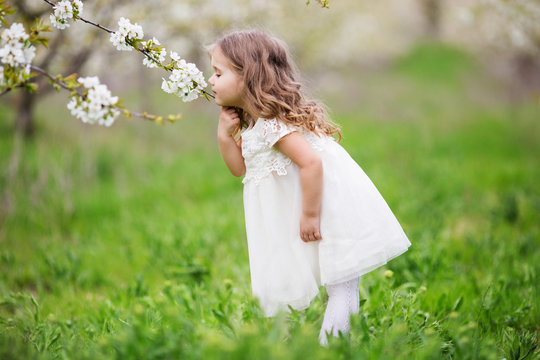 Pretty Child Girl Is Smelling Flowers In Garden