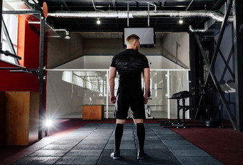 Young man preparing muscles before training, back view . Muscular athlete exercising crossfit. Workout lifestyle concept