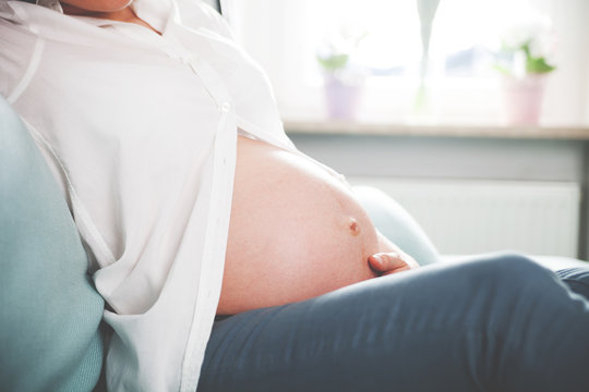 Pregnant woman sitting on sofa at home close up of belly