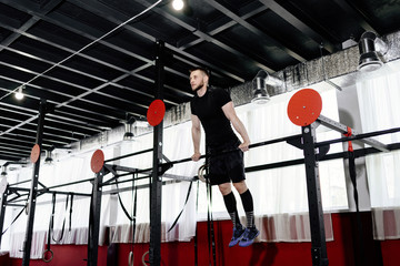 Young man exercising on horizontal bar in the gym. Male adult working out triceps and biceps on horizontal bar as crossfit training