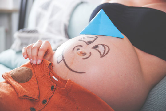 Close up of pregnant belly with happy smiley face and clothes for baby