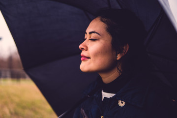 Beautiful girl with dark hair breathing in spring air under the umbrella