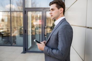 Fototapeta premium Businessman holding mobile smartphone using app texting sms message wearing suit jacket outdoors near office building.