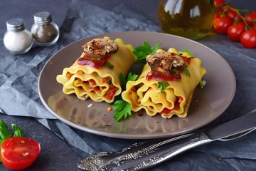 Pasta rolls with vegetables: paprika, onion, olives, mushrooms, tomato, glass jar with olive oil on a light brown plate on a grey abstract background. Vegetarian food. Dieting. Mediterranean lifestyle