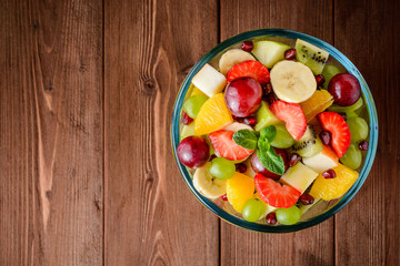 Healthy fresh fruit salad in glass bowl on wooden background.