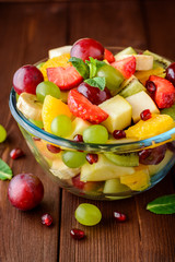 Healthy fresh fruit salad in glass bowl on wooden background.