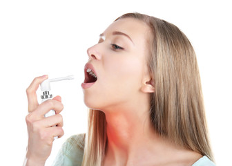 Sick young woman using throat spray on white background