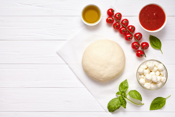 Raw pizza dough with ingredients: mozzarella, tomatoes sauce, basil, olive oil, cheese, spices. Italian margherita on wooden table. Italian pizza margarita