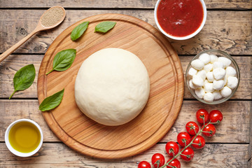 Pizza cooking ingredients on cutting board. Dough, mozzarella, tomatoes, basil, olive oil, spices. Work with the dough. Top view. Flat lay. Traditional italian pizza margherita.
