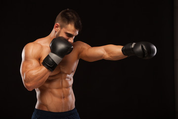 Plakat Muscular young man with perfect Torso with six pack abs, in boxing gloves is showing the different movements and strikes isolated on black background with copyspace