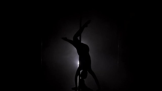 Young slim woman's silhouette dancing on the pole upside down