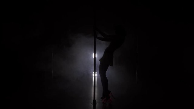 Young slim woman's silhouette dancing near the pole in the studio